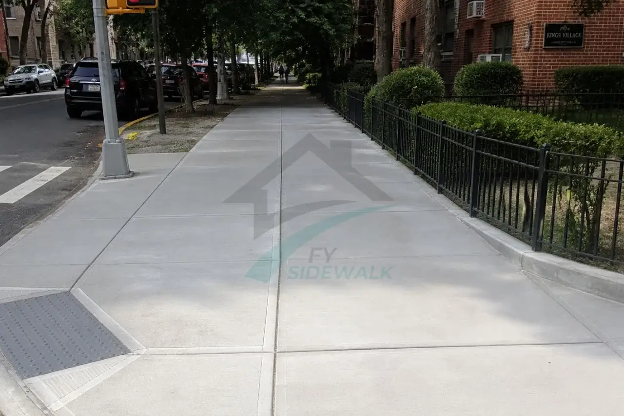 new concrete sidewalk with a tactile pedestrian ramp outside a brick apartment building in brooklyn