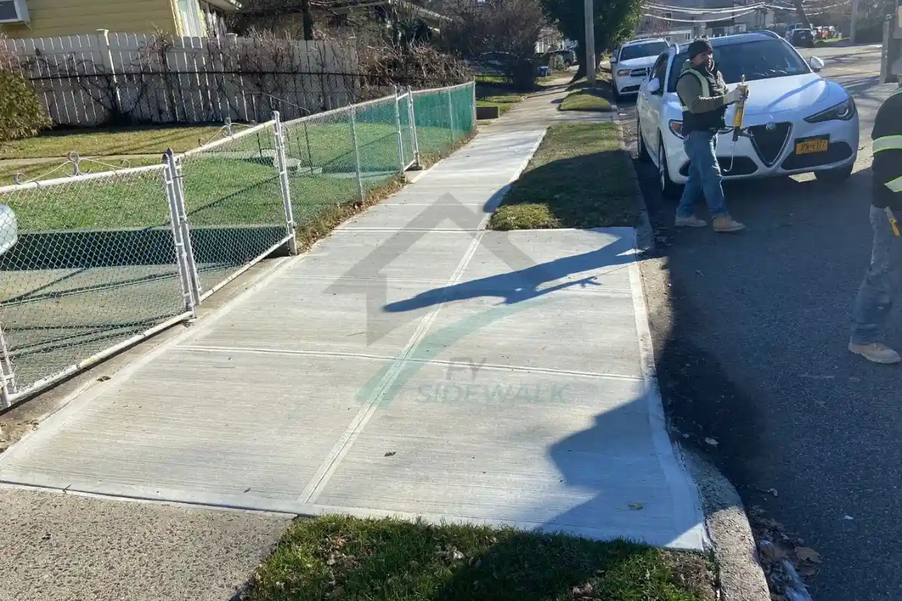 newly poured concrete sidewalk beside a residential fence in nyc with an fy sidewalk crew finishing the joints