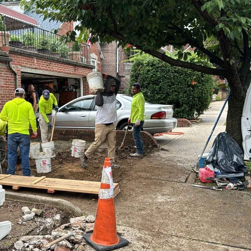 sidewalk repair crew fixing cracked and uneven concrete slabs in queens neighborhood